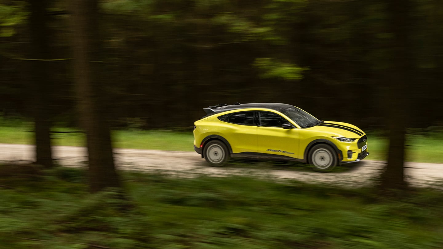 Ford Mustang Mach-E Rally in Gelb. Seitenansicht, fahrend durch einen Wald.