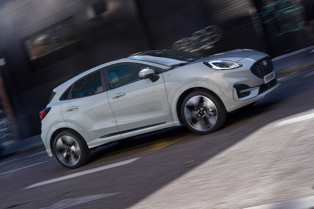 Ford Puma in Grau. Seitenansicht, fahrend durch die Stadt.