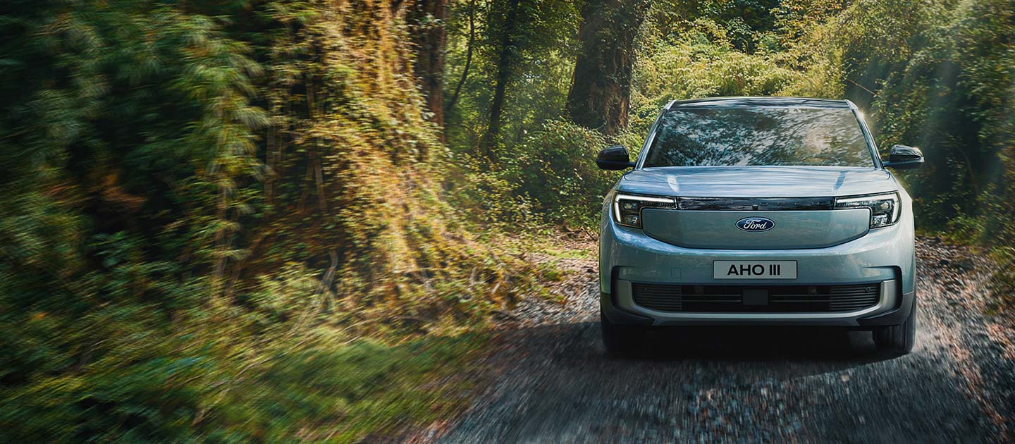 Der vollelektrische Ford Explorer in Blau. Heckansicht, fahrend durch einen Wald.