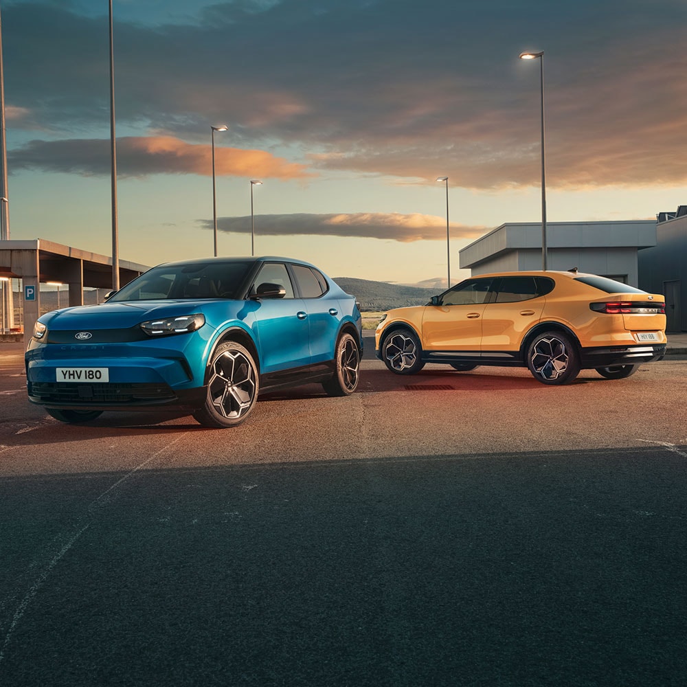 Ford Capri in Gelb und Blau auf einem Parkplatz bei Sonnenuntergang.